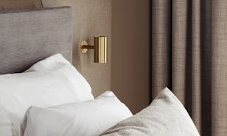 Ett mysigt sovrum med en säng, kuddar och varm belysning från en hängande sfärisk lampa och en väggmonterad lampa. Gardiner är fördragna.