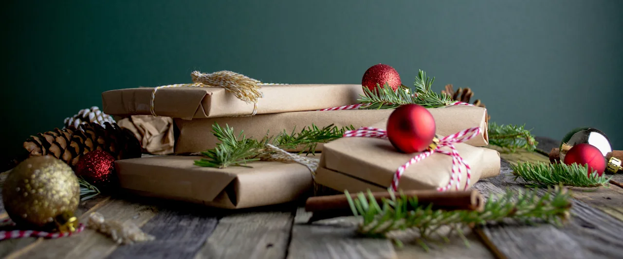Julegaver innpakket i brunt papir med festlige dekorasjoner på et rustikt trebord, mot en mørkegrønn bakgrunn.