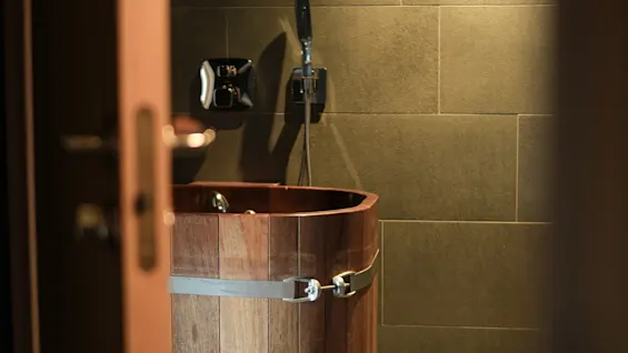 Et tønneformet badekar i tre med metallbånd, sett fra en åpen dør, i et flislagt bad.