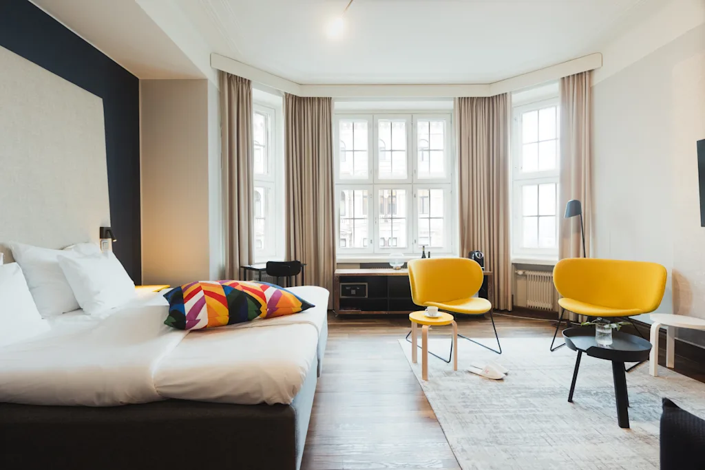 Henkilö kylpytakissa nauttii aamiaista sängyssä ja katselee maisemaa hotellihuoneen ikkunasta.