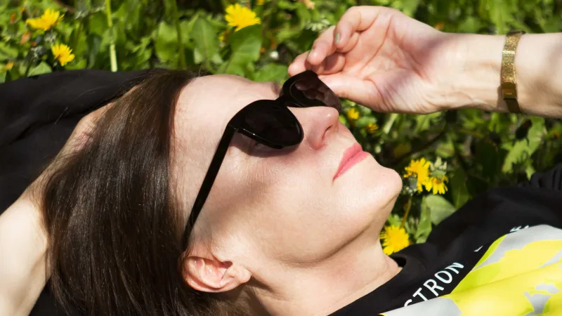 A woman wearing sunglasses lying in a field full of dandelions.