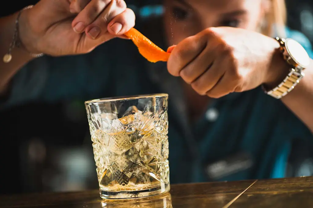 Bartender squeezing orange zest on drink