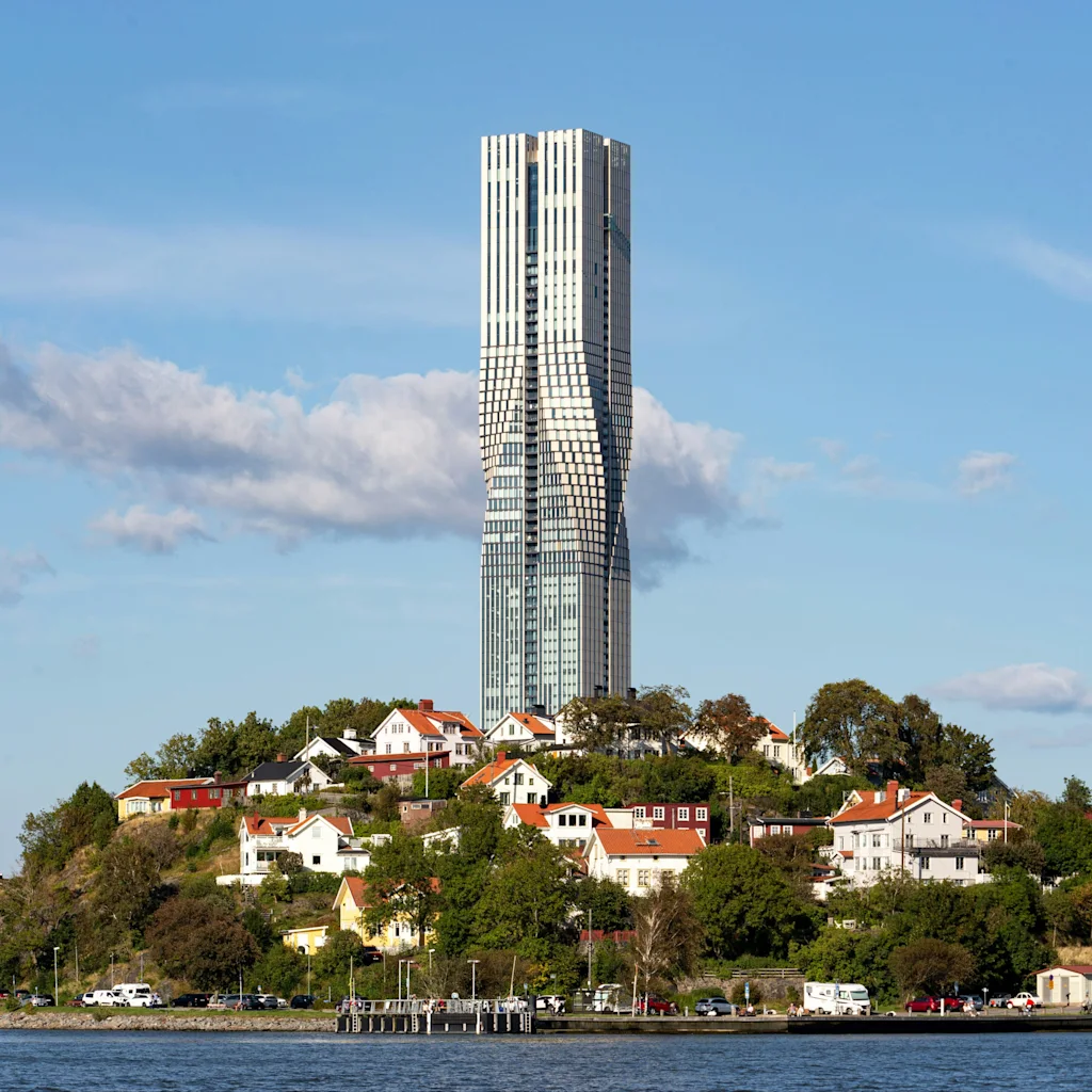 Karlatornet i Gøteborg, en moderne vridd skyskraper, ruver over tradisjonelle hus på en grønn ås ved vannet.