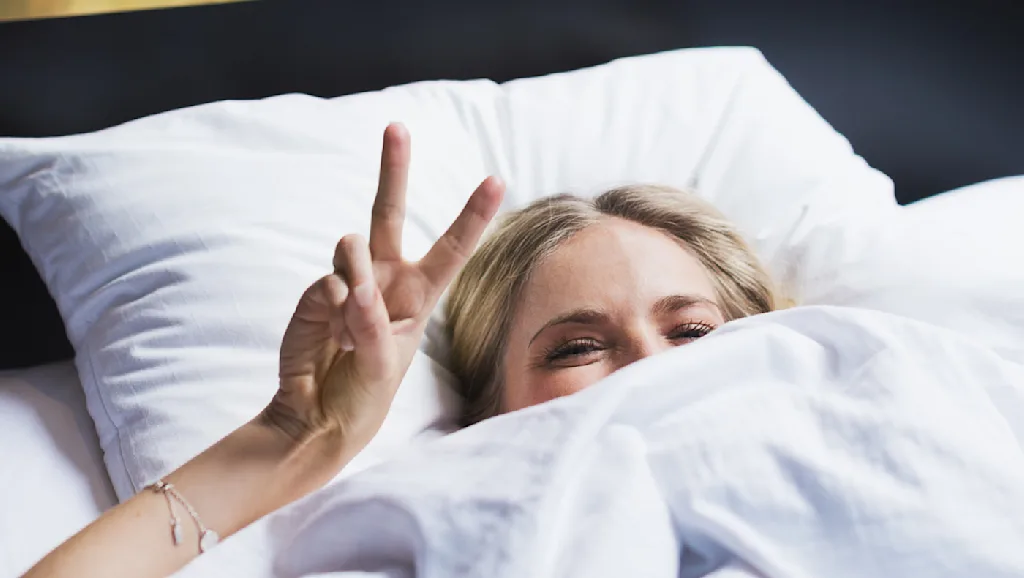 Woman in hotel bed showing the peace sign