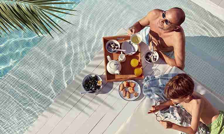 Man and child eating breakfast by the pool