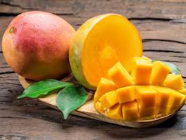 A vibrant, ripe mango shown both whole and cut in the distinctive cross-hatch pattern popular for dog-safe serving, displayed on a rustic wooden board with fresh green mango leaves,