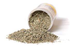 A close-up of a dried catnip herbs spilling out of a jar onto a white surface, commonly used for cats.