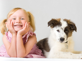 Smiling blonde girl in pigtails posing with a playful black-and-white puppy, perfect for inspiring funny dog names based on their adorable and joyful expressions.