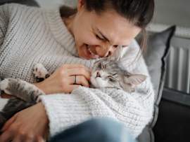 A smiling woman cuddles a relaxed gray tabby cat nestled contentedly in her arms, the kind of bond that's possible when you learn how to desensitize a cat to being picked up and held. This cozy moment is a perfect example of what it looks like when you've figured out how to get a cat to be comfortable with you during close contact.