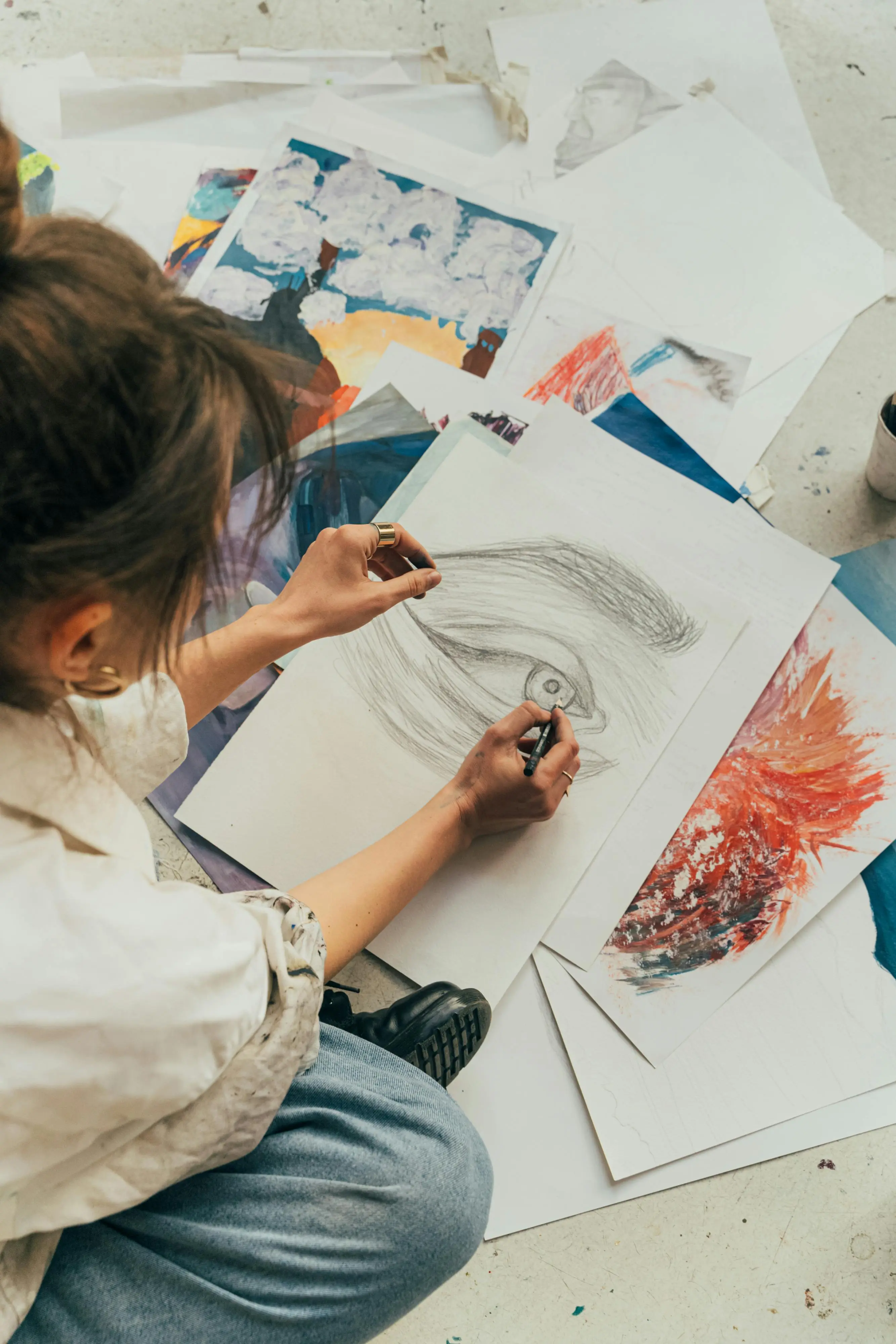 Artist Using Art for Expression and Healing Person sitting on the floor surrounded by artwork, sketching an image of an eye.