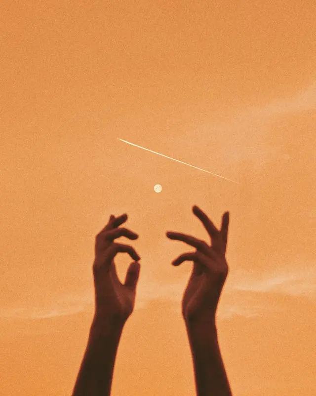 Experiencing Peace While Connecting to Nature A pair of silhouetted hands reaching towards the orange sky at sunset, symbolizing hope in mental health recovery.