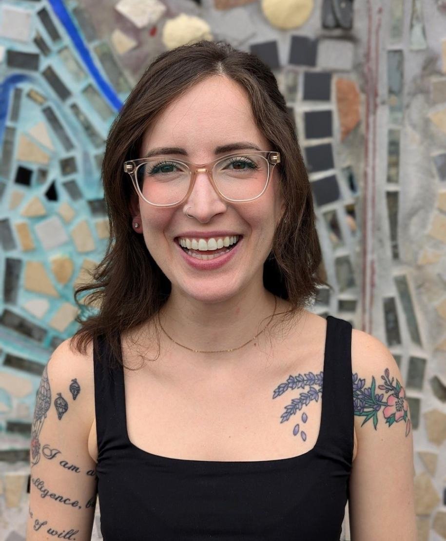 Gianna Damis ATR-BC LPC Therapist A photo of Gianna Damis, owner of Created Self Therapy, standing against a mosaic mural looking into the camera and smiling.