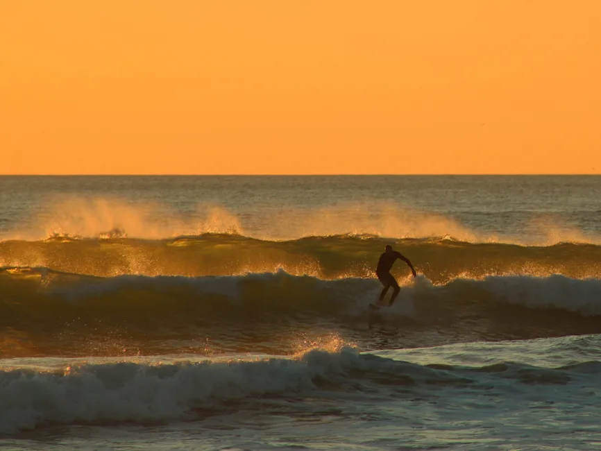 Man surfing at dusk | A man surfing small waves at dusk.