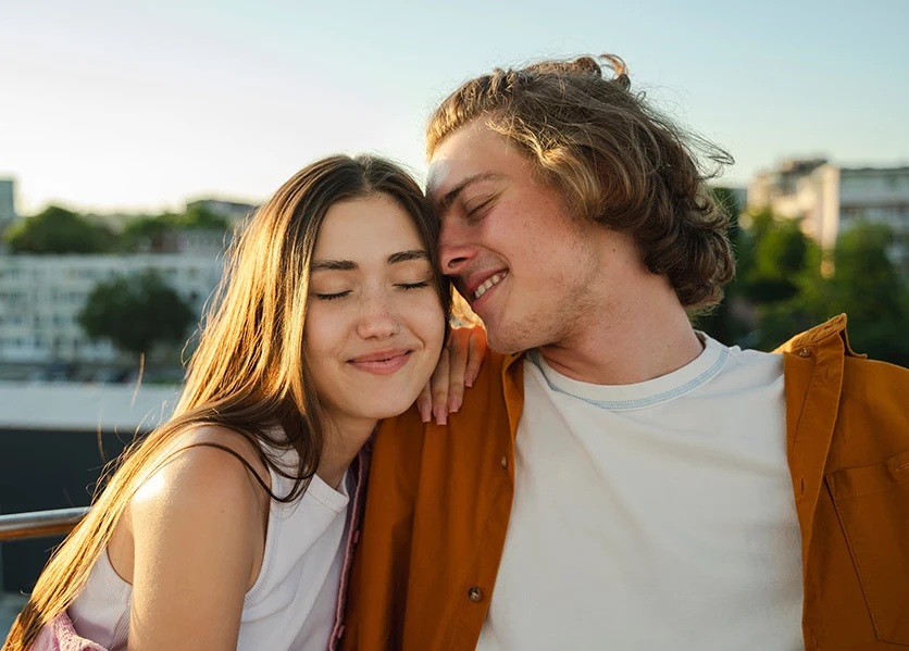 Femme aux cheveux bouclés et homme barbu dos à dos, souriants