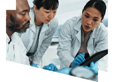 Three researchers wearing lab coats focused on a tablet in a lab environment.