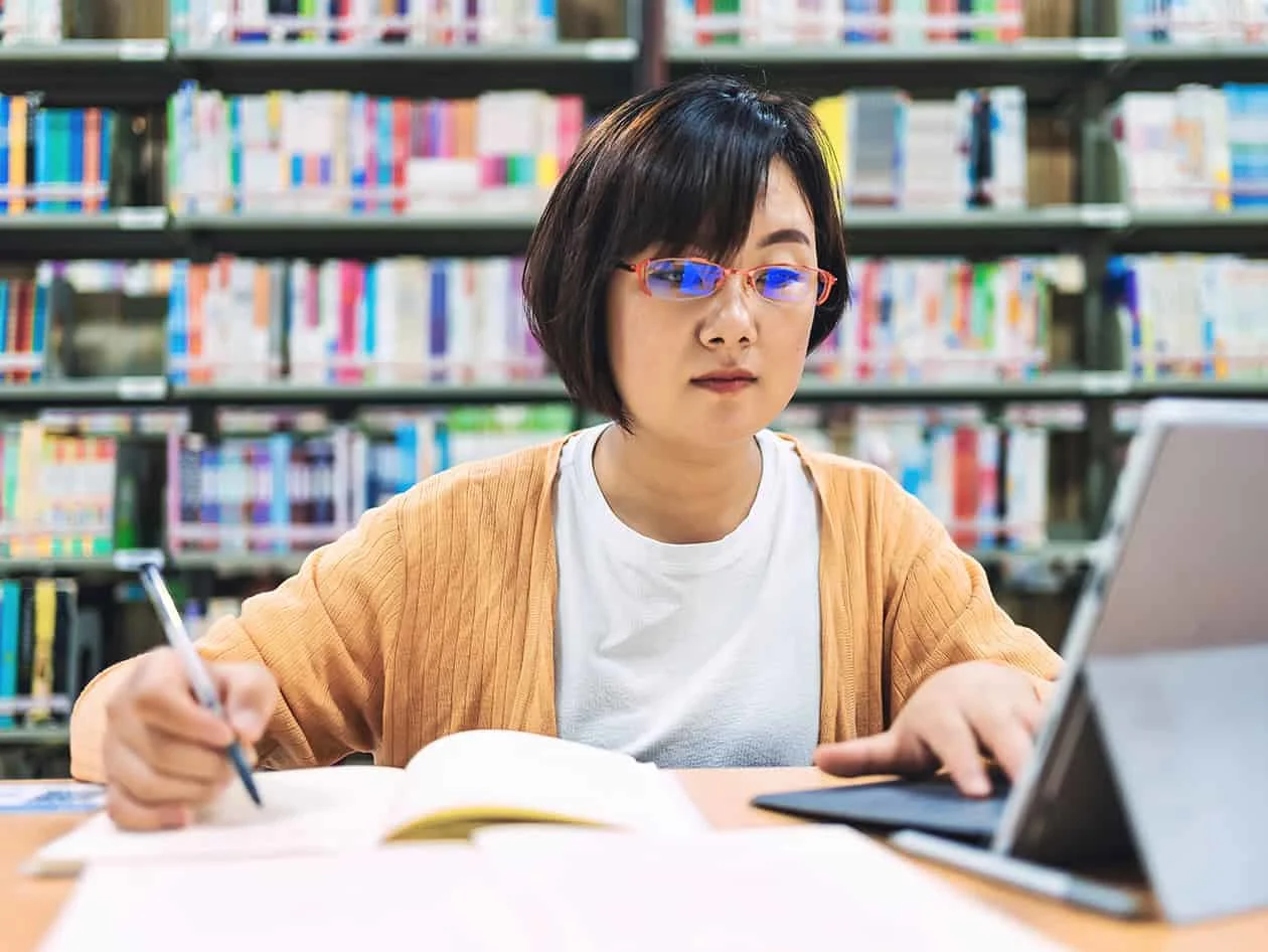 Woman in a library studying using books and a laptop