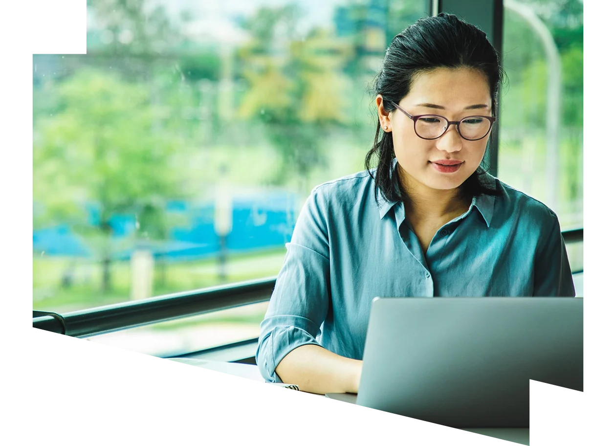 A woman sitting at a desk, working on a laptop with a pen in her hand.