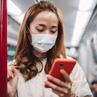 Woman wearing facemask with smartphone on train 