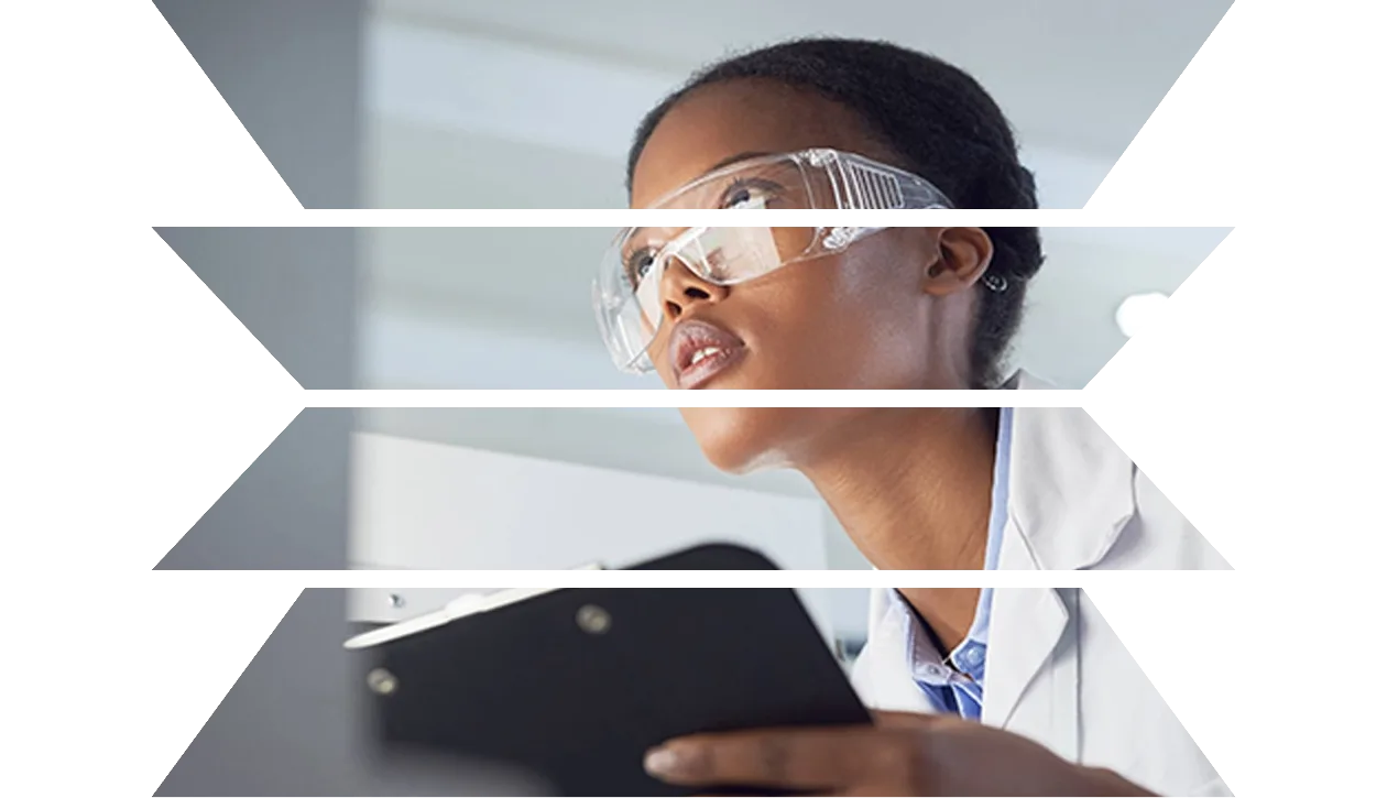 Female scientist wearing goggles looking at computer holding clipboard