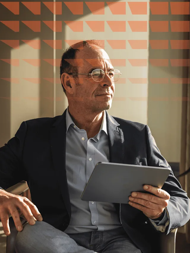 Man in a suit holding a tablet while looking far away.