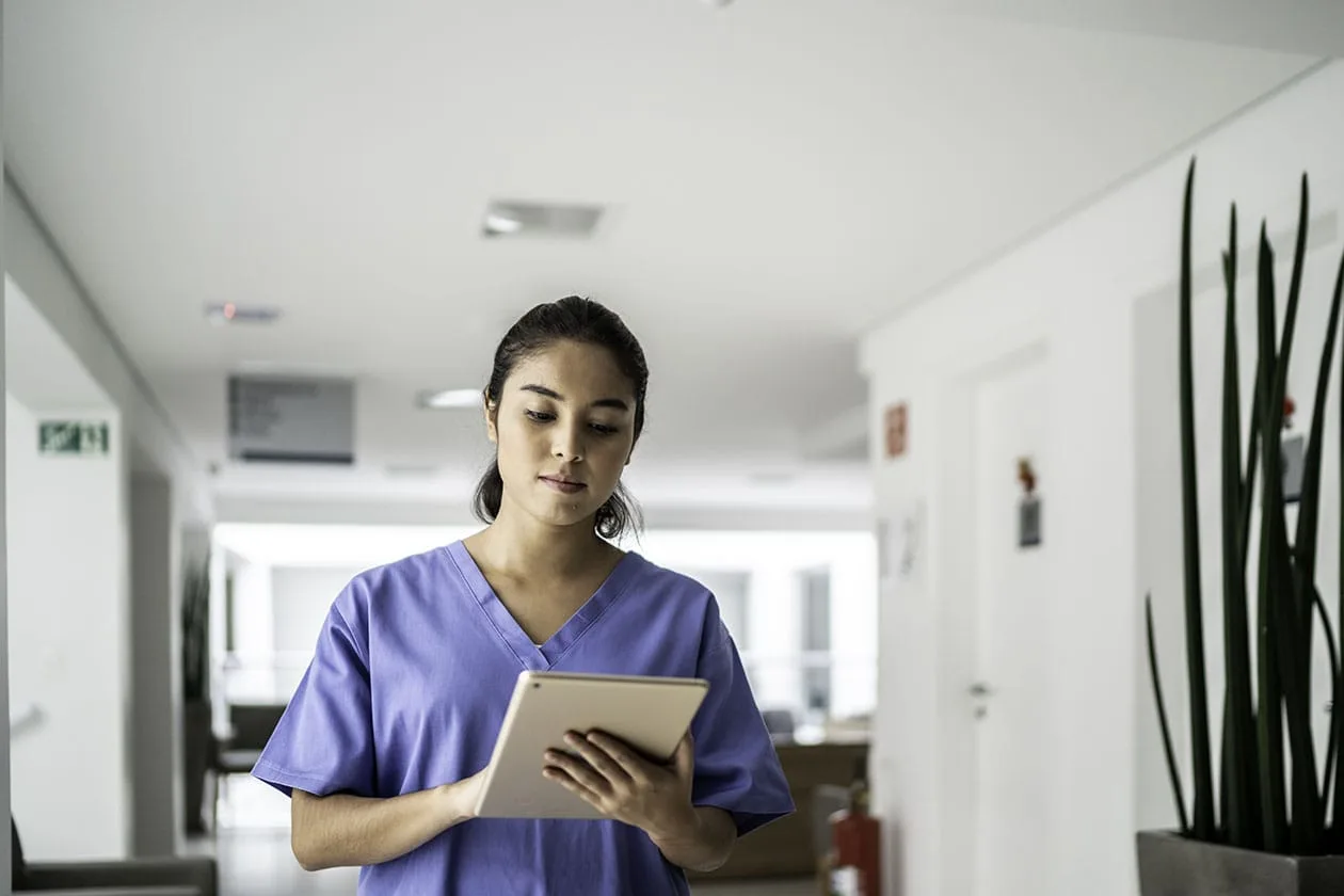 Young female nurse in scrubs reviews information on a tablet.