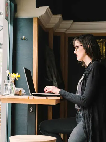 Woman on laptop standing next to window