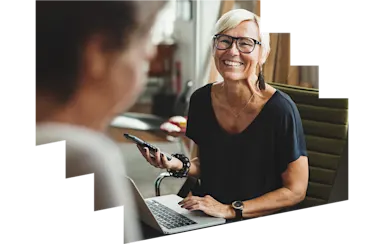 Woman with a laptop and phone smiling at a colleague