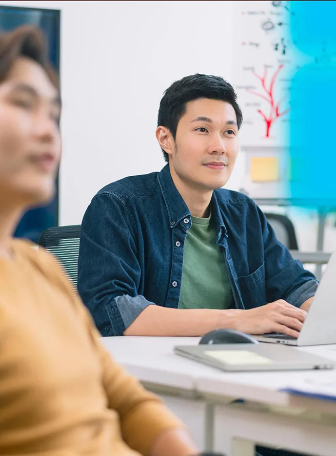 A man in a lab coat points at a screen displaying graphs and data.