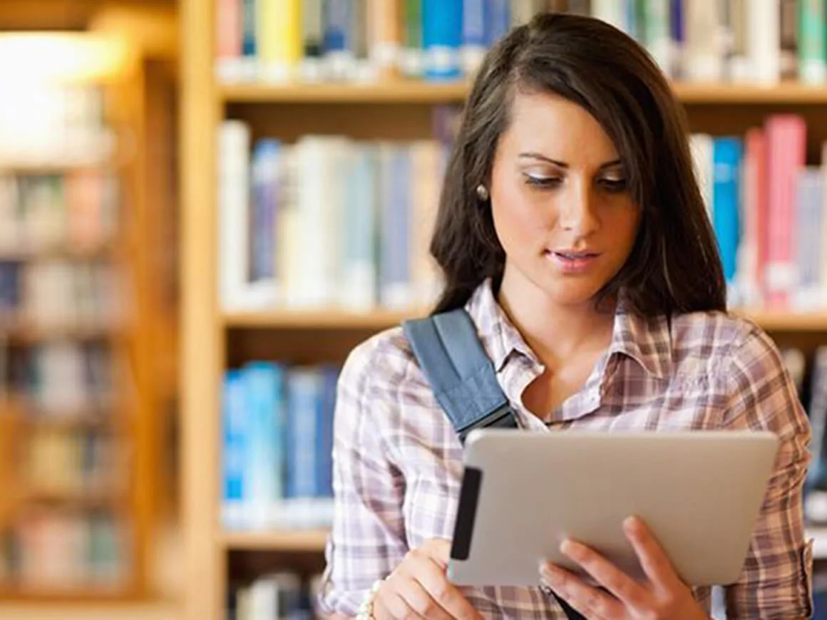 Mujer joven en la biblioteca sosteniendo una tableta