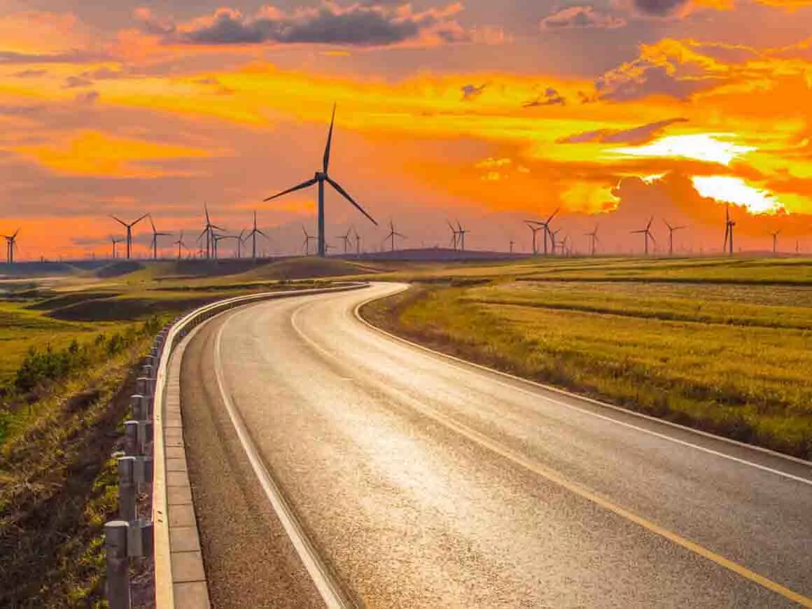 Winding road at sunset with wind turbines at the horizon