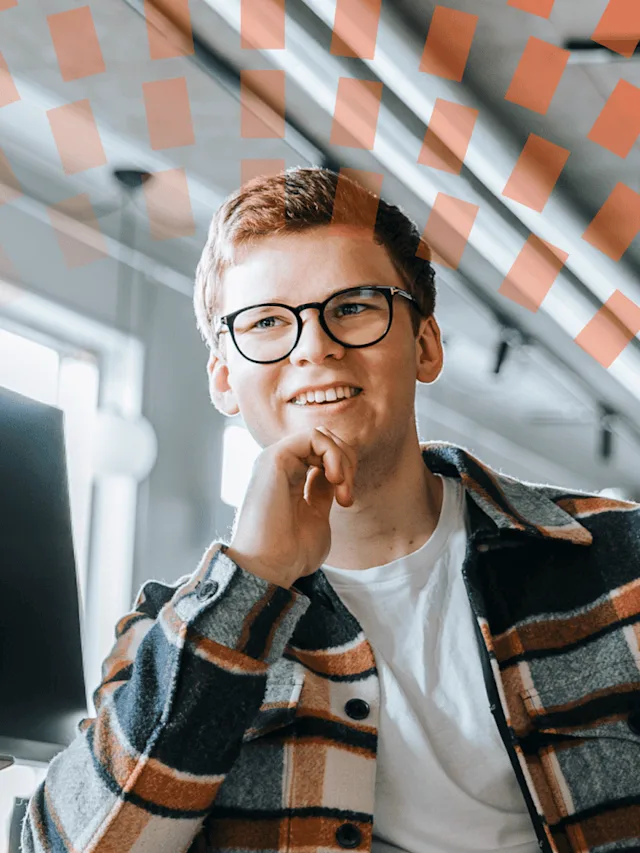 A smiling young man wearing glasses in an office setting.