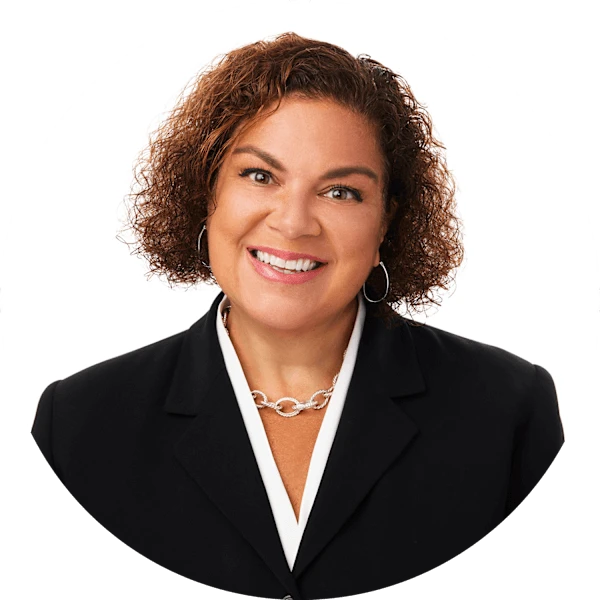 A woman with short, curly brown hair smiles at the camera. She wears a white blouse and black jacket.