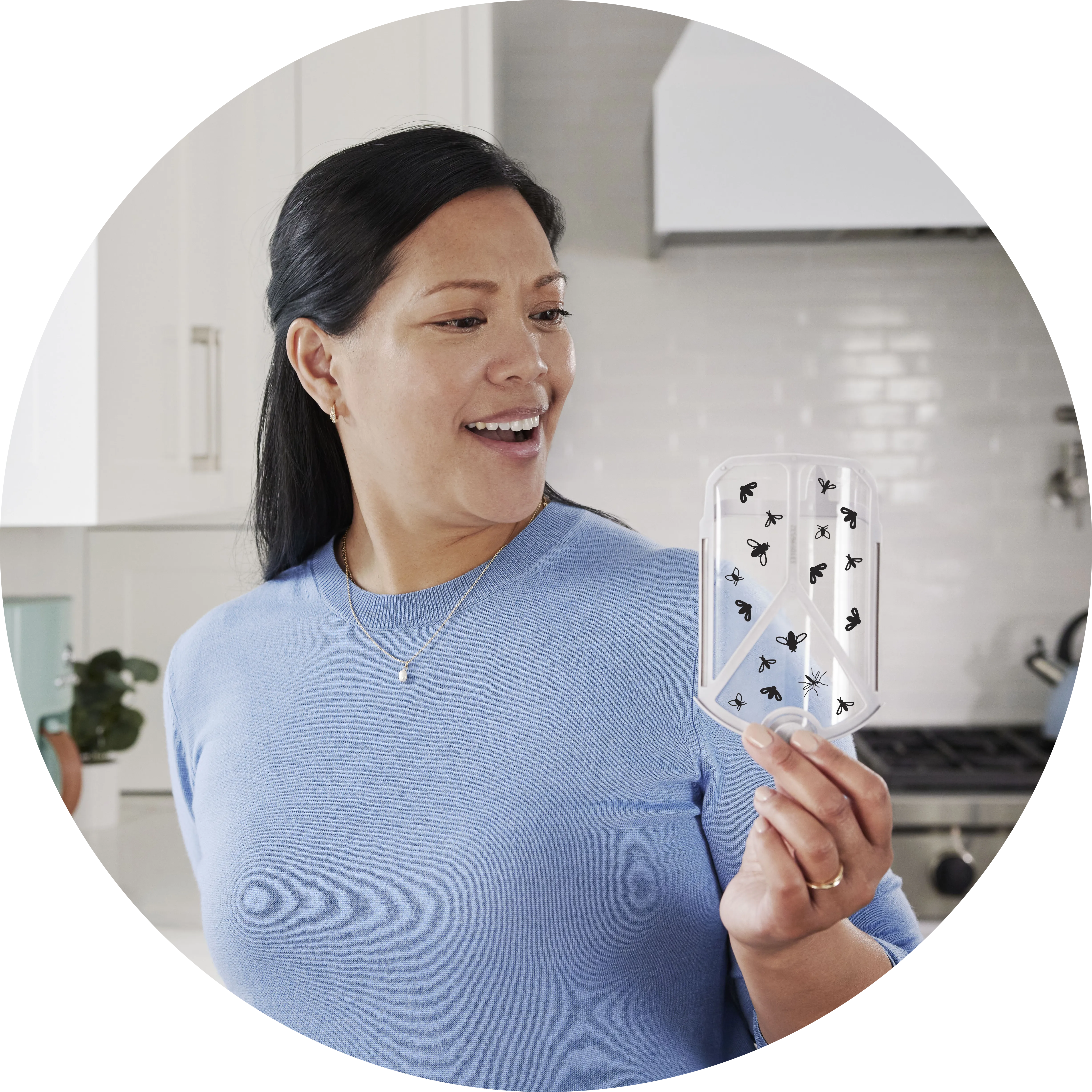 An Asian woman stands in a kitchen. She holds up a clear cartridge for an insect and bug device.