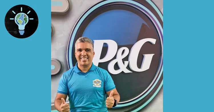 Hispanic man with grey hair and a blue shirt stands in front of a P&G sign that hangs in the background.