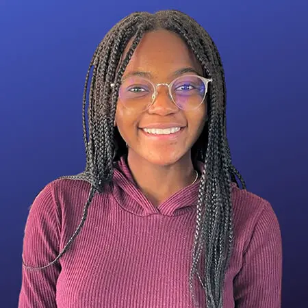 A young black girl with long, dark braids and round light-colored glasses smiles and poses for a headshot.
