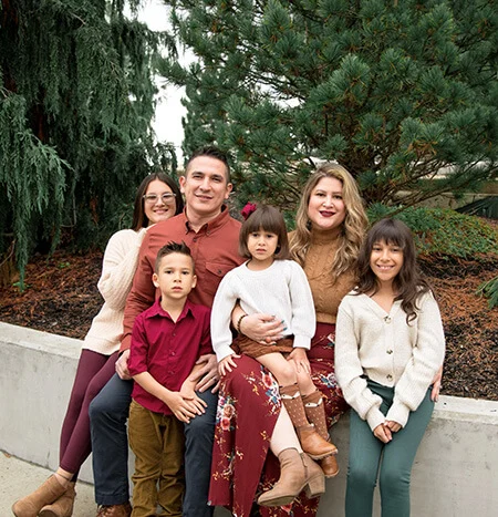 An adult male with short dark hair and an adult female with long blonde hair pose with their children - three young girls and a young boy.