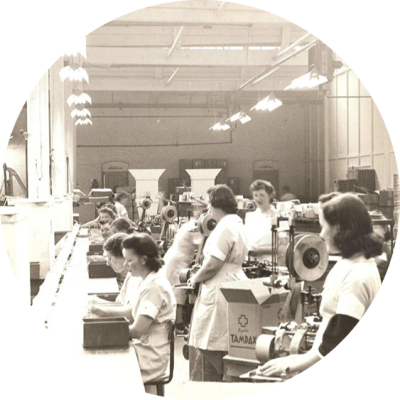 Several white women in uniforms are working in a Tampax factory during world war two. The image is in black and white.