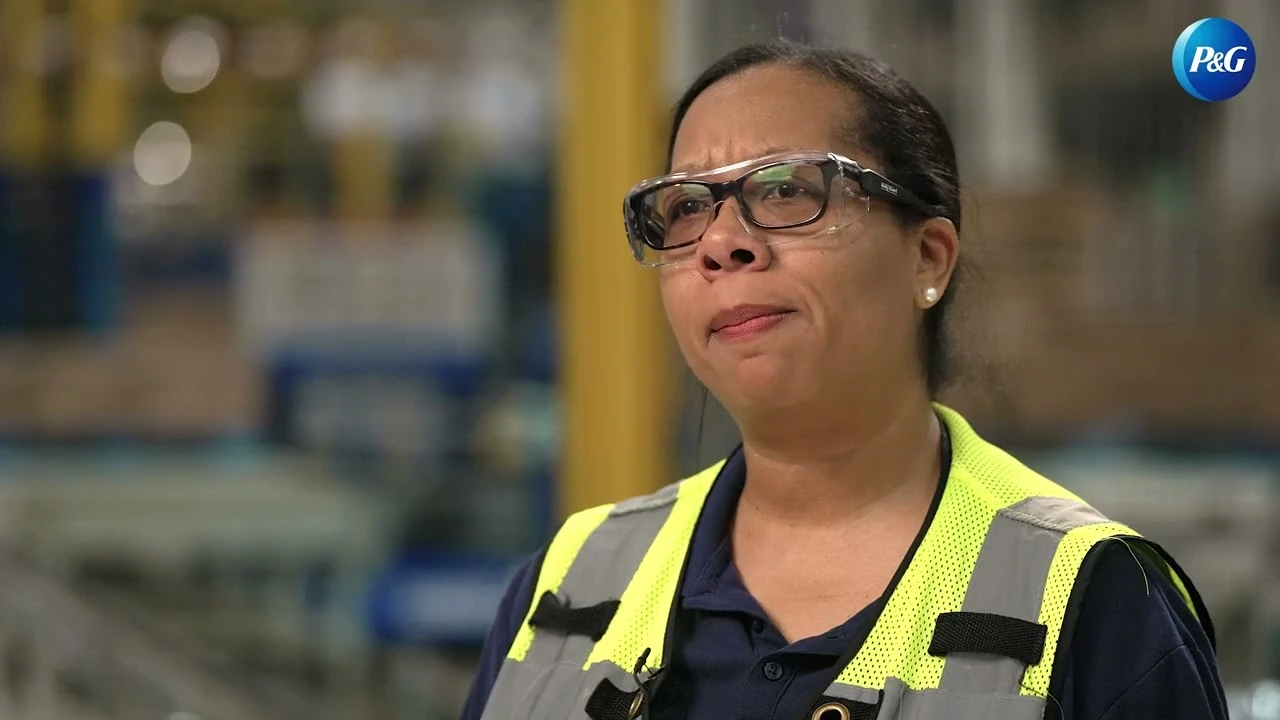 Employee wearing safety vest speaking in warehouse with stacked pallets