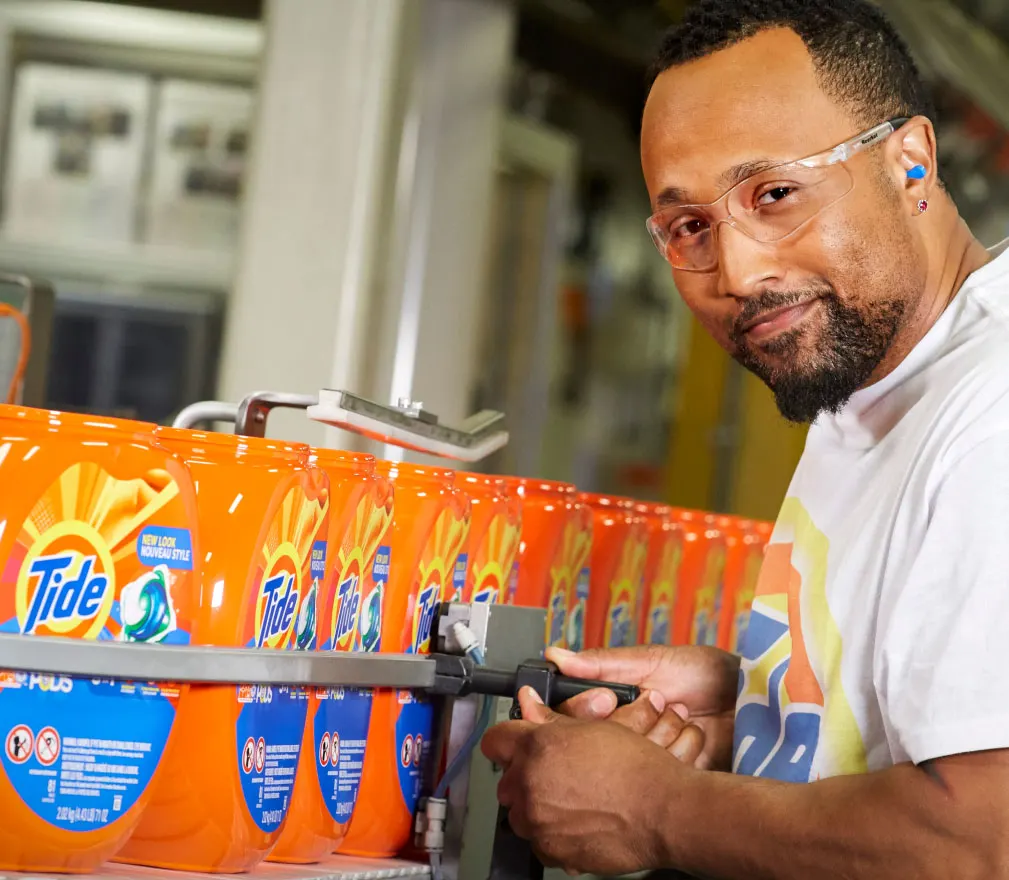 Man in a manufacturing facility next to many Tide product bottles