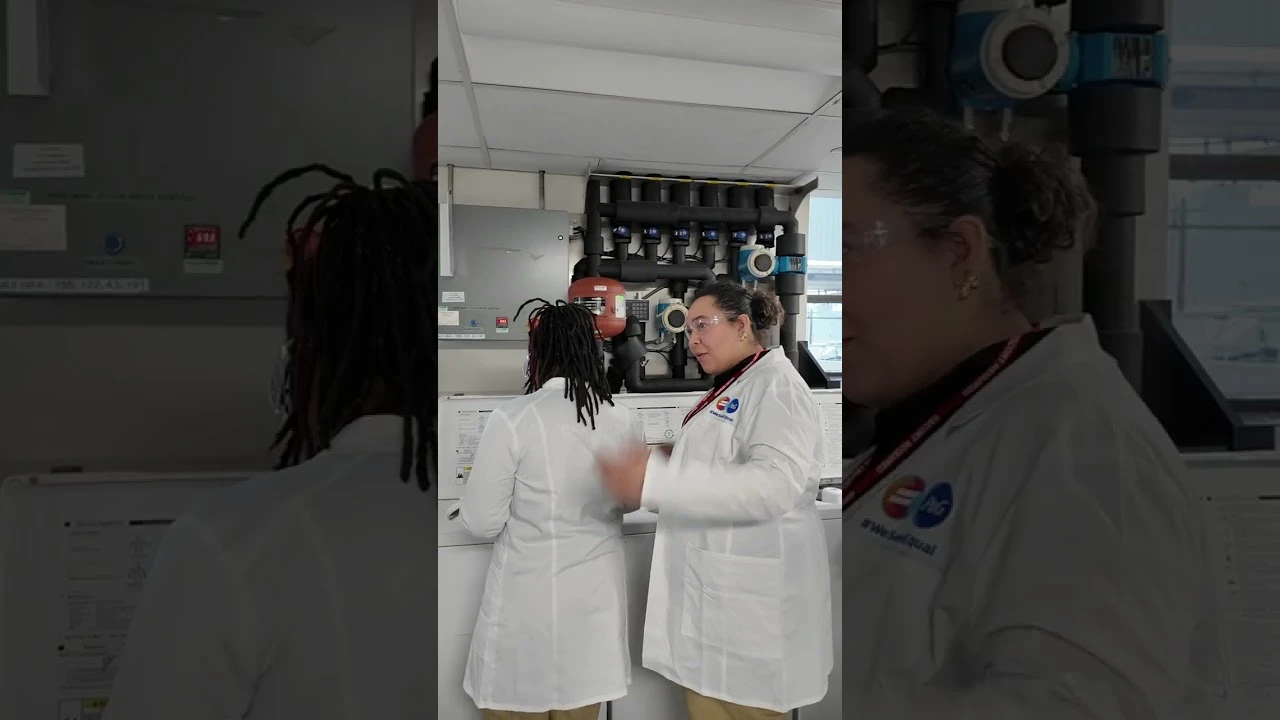 Women in lab coats working together at a laboratory workstation with industrial equipment.