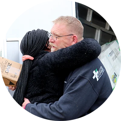 A man and a woman hug. They stand in front of a delivery truck filled with paper towels and personal care products.