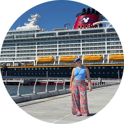 A young woman in a blue shirt and colorful plants stands on a long runway in front of a large cruise ship.