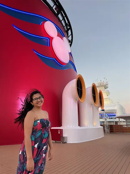 A woman in a colorful dress stands in front of a large red and white structure on a cruise ship.
