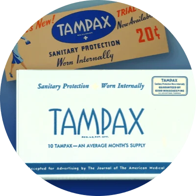 A white box top with blue text displays "Tampax." Another brown box top includes colored text and an illustration of a woman in a blue skirt suit. Both boxes are historical versions of Tampax packaging. A full page magazine clip sits on the right.