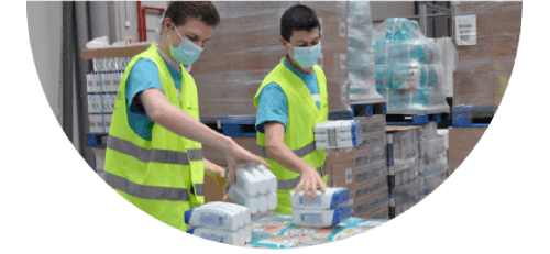 Two men wearing masks and high-visibility safety vests handle P&G products inside a warehouse