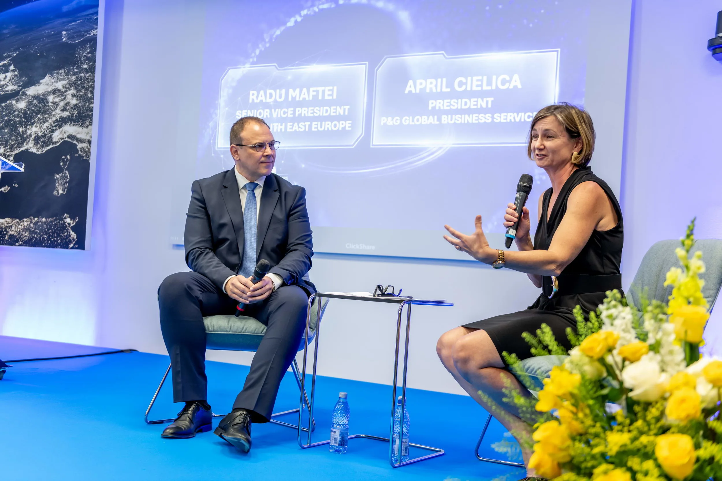 A formal event where a man in a suit holds a microphone while listening to a woman in a black dress who is actively speaking into her own microphone