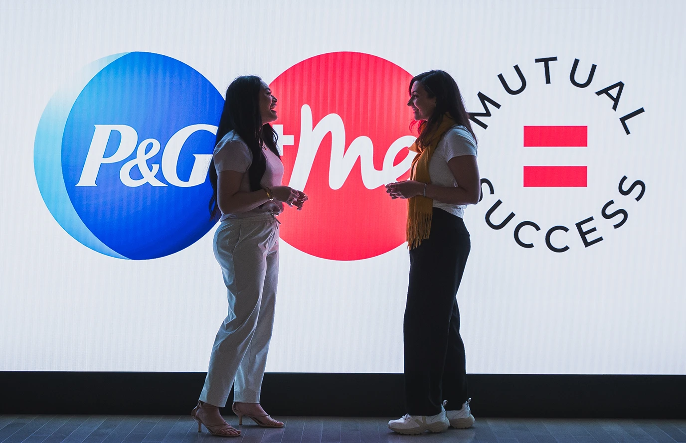 Silhouettes of two women standing before an illuminated P&G sign.