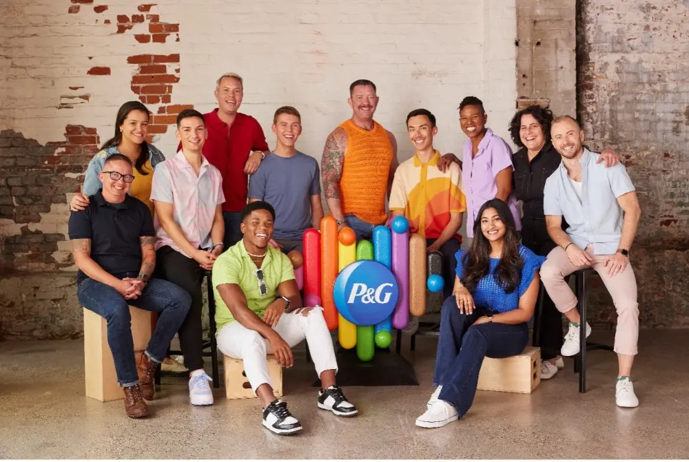 Twelve employees are standing and sitting around a Procter and Gamble rainbow heart statue.