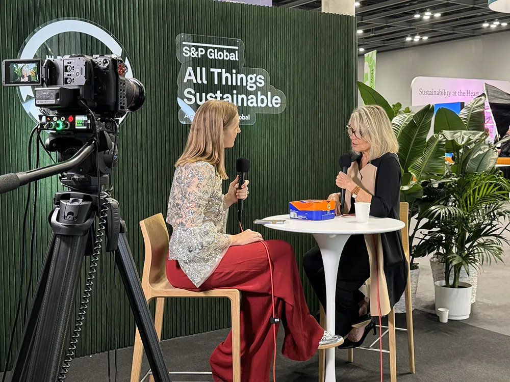 Two women with microphones sit at a table recording a podcast