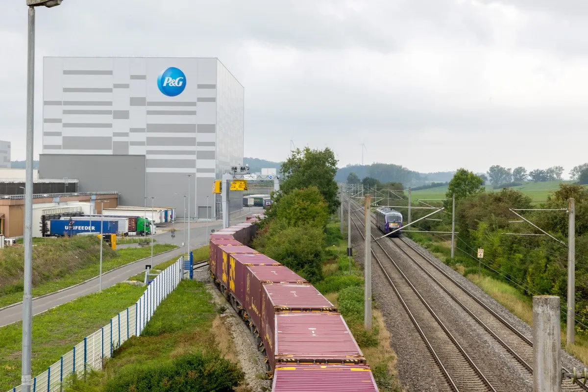 Trains on a rail line headed towards the P&G Crailsheim facility which is visible in the background.